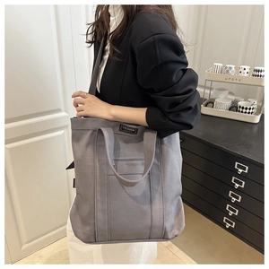 Detail view of grey canvas tote bag with fashion label shown on model for daily commute