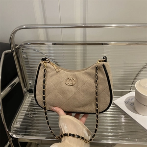 Quilted beige underarm bag with black trim and elegant metal chain strap held by hand