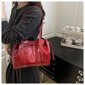 Detail of red patent leather tote bag featuring a decorative bow and drawstring closure
