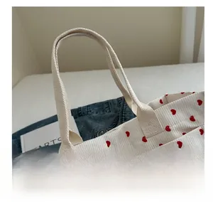 Detail of reinforced handles on a corduroy tote bag with red heart patterns