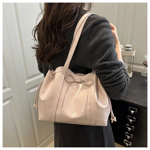 Detail of pink patent leather tote bag featuring a bow decoration and side drawstring design