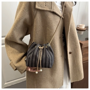 Mini woven bucket bag with pearl drawstring and golden chain detail on beige coat