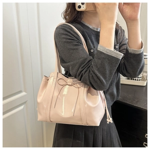 Detail of light pink patent leather tote bag with glossy finish and ribbon bow design