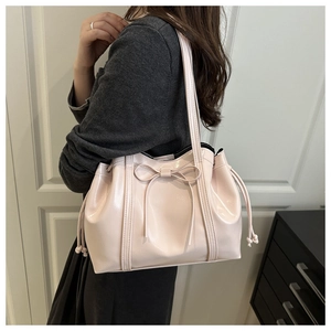 Detail of light pink patent leather tote bag featuring a decorative bow and drawstring side