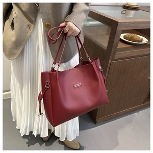 Dettaglio di una borsa tote bordeaux in pelle con trama a grana di litchi e logo fashion