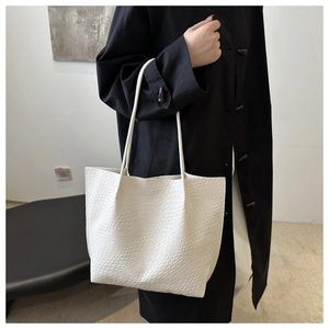 Detail of white embossed tote bag showing woven texture on a minimalist shoulder handbag