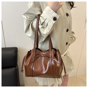 Detail of glossy brown tote bag with bow accent and drawstring side cinching feature