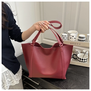 Detailed side view of a large vintage burgundy leather tote bag held by a person indoors