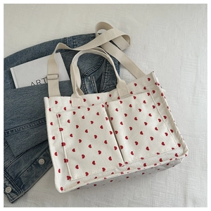 Detailed view of cream corduroy tote bag featuring red heart patterns and dual front pockets