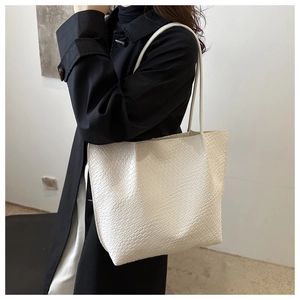Detailed close-up of a white woven texture tote bag on a model shoulder with black coat