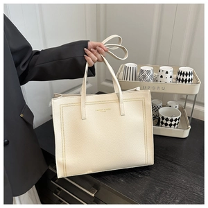 Detail of cream tote bag in lychee leather texture with gold foil stamped letters