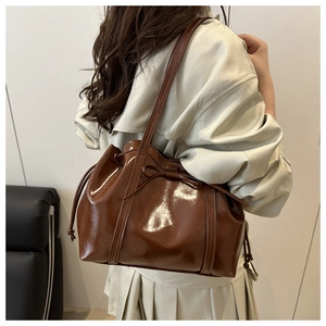Close-up of brown glossy bucket bag with bow drawstring and sleek shoulder strap