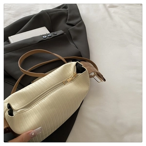 Close-up of beige handbag featuring vertical pleated texture and brown leather strap