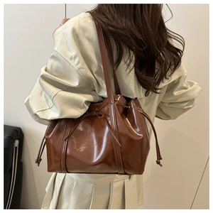 Brown oil wax leather tote bag with bow drawstring detail worn with a beige trench coat