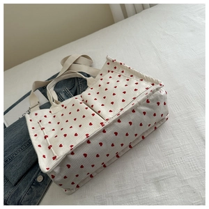 Detail of white corduroy tote bag featuring red heart patterns and dual front pockets
