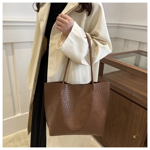 Detailed view of brown woven tote bag showing Intrecciato texture on woman shoulder