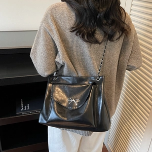 Sac fourre-tout moderne en similicuir noir avec nœud argenté et chaîne porté par un mannequin