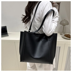 Minimalist large black leather tote bag shown in use on a model in a modern home office