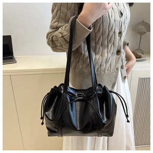 Detail of glossy black tote bag featuring a decorative bow and drawstring accents