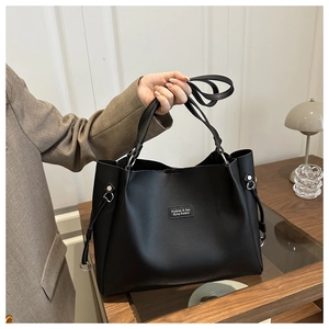 Dettaglio di borsa tote in pelle nera con logo minimalista e fibbia laterale in metallo