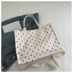 Detail of white corduroy tote bag featuring red heart prints and long shoulder strap