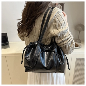 Detail of black glossy leather tote bag showing decorative bow and drawstring texture