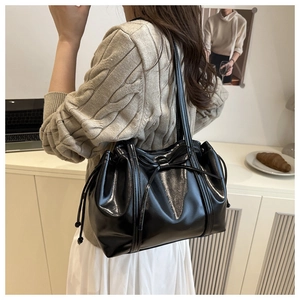 Detail view of black glossy leather tote bag featuring a bow tie and drawstring closure