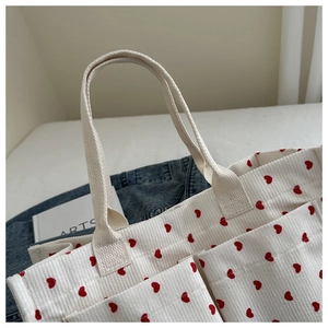 Detailed close-up of white corduroy tote bag with red heart pattern and dual pockets