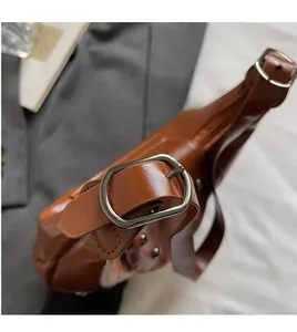 Detail of adjustable metal buckle and smooth brown leather texture on shoulder bag