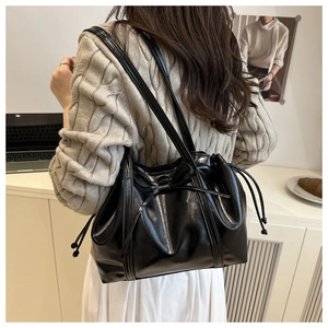 Detail of a black shiny leather tote bag with bow decoration and double shoulder straps