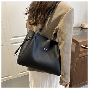 Dettaglio borsa tote in pelle nera con logo rettangolare minimalista e finiture in metallo dorato