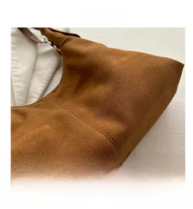 Detail view of brown suede texture with fine stitching and silver metal buckle on handbag