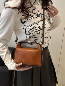 Retro contrast color handbag with orange pleats and dark brown leather strap worn by model