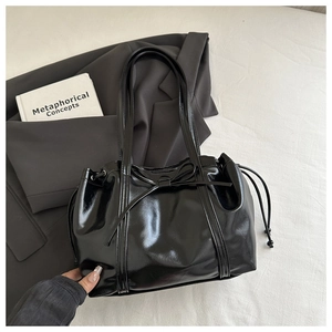 Detail of black glossy tote bag with drawstring closure and bow decoration on white fabric