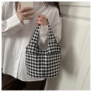 Detail of checkered canvas tote bag with front pocket held by model in casual outfit