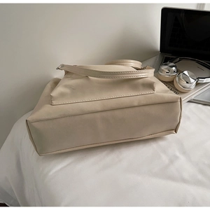 Détail d'un sac cabas en similicuir beige posé sur une surface blanche avec accessoires
