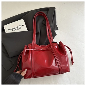 Detail of red patent leather tote bag featuring a bow decoration and drawstring closure