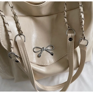 Détail du sac cabas crème avec logo nœud en métal argenté et bandoulière en chaîne
