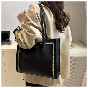 Detail view of large black tote bag with gold stud trim and elegant pebbled leather texture
