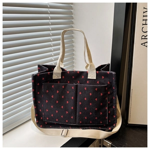 Detail of black corduroy tote bag with red heart pattern and dual front pockets