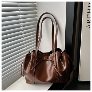 Detail of dark brown glossy shoulder bag with bow decoration and adjustable drawstrings