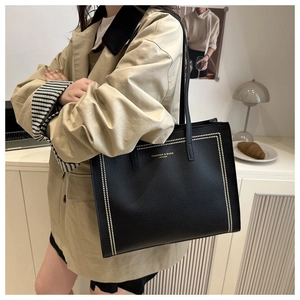 Chic black tote bag with gold rivets and leather texture worn with a trench coat