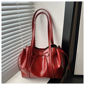 Detail of red glossy patent leather tote bag featuring a 3D ribbon bow decoration