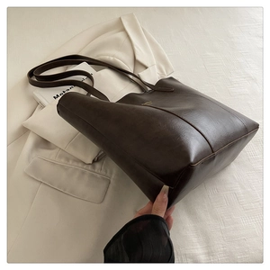 Detailed macro view of dark coffee leather texture and gold logo on the tote bag
