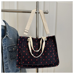 Detail of corduroy tote bag featuring red heart patterns and adjustable cream shoulder strap