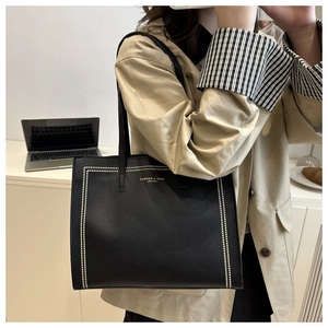 Detail of black pebbled leather tote bag featuring gold stud trim and shoulder straps