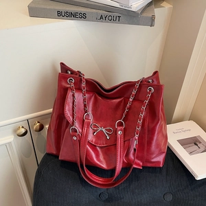 Détail du cabas rouge avec nœud en métal argenté et bandoulière chaîne sur chaise
