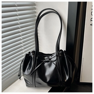 Detail view of glossy black tote bag featuring a decorative bow and drawstring closure
