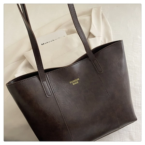 Close-up of dark brown tote bag with oily texture and gold FASHION BAGS lettering