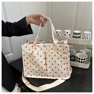 Detail of cream corduroy tote bag featuring red heart patterns and front patch pockets